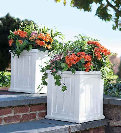 A set of white Lexington self-watering planters with flowers on a patio