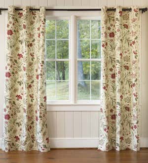 A window with grommet-top curtains with a Jacobean floral pattern in red and sage green.