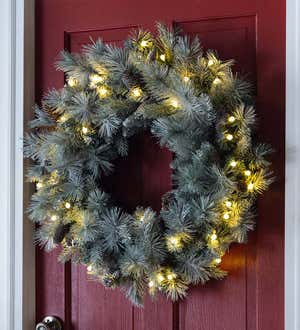 A lighted frosted evergreen Christmas wreath on a red door