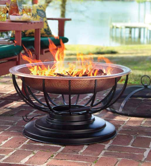 A Hammered Copper Fire Pit with a roaring fire sits on a brick patio