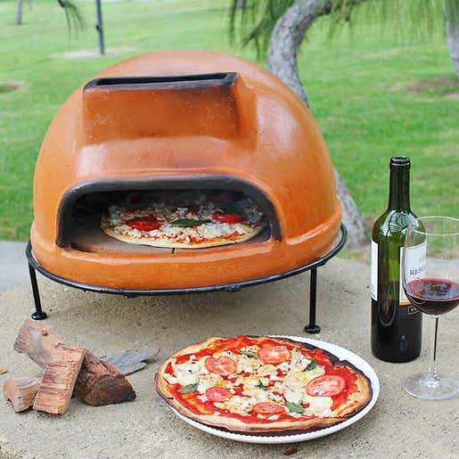 An Authentic Talavera Liso Pizza Oven sits outdoors with a wood-fired pizza