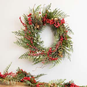 A Chesterfield Iced Pines wreath with red berries and ferns over a mantel