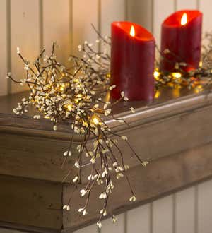 Lighted red berry garland and pillar candle on a mantel
