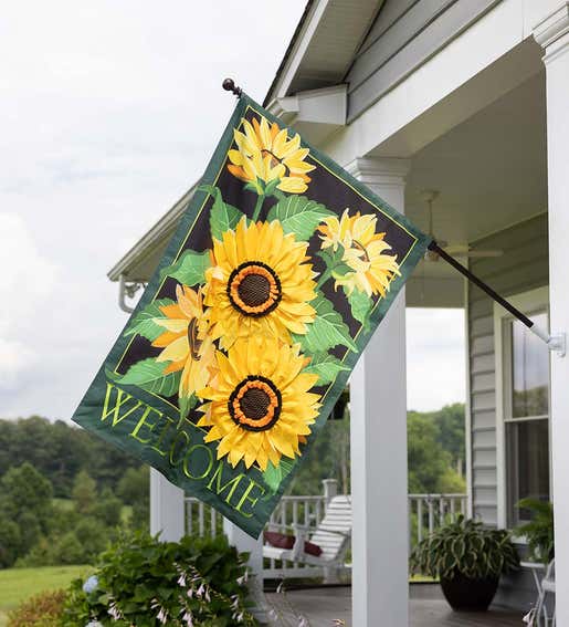 A large estate house welcome flag with sunflowers hangs from a front porch