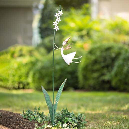 A whimsical metal fairy garden stake in a flower bed
