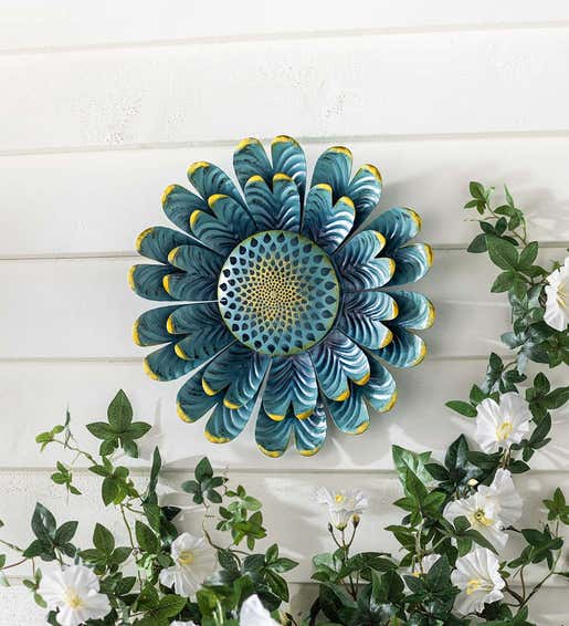 A metal wall art piece of a large blue and yellow flower hangs on a porch wall